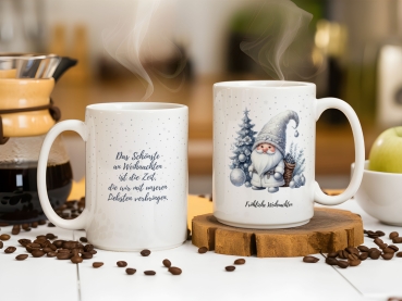 Preview: Personalisierte Weihnachtstasse mit Zitat Preview: Zwei weiße Weihnachtstassen stehen auf einem weißen Tisch, umgeben von Kaffeebohnen und einer Kaffeemaschine im Hintergrund. Die linke Tasse zeigt den Text
